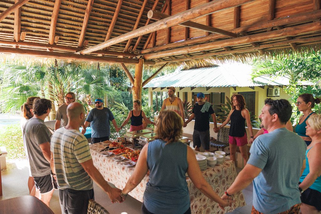 CLQ retreat participants holding hands in a circle before a shared meal, symbolizing community, connection, and integration during a leadership retreat in Costa Rica.